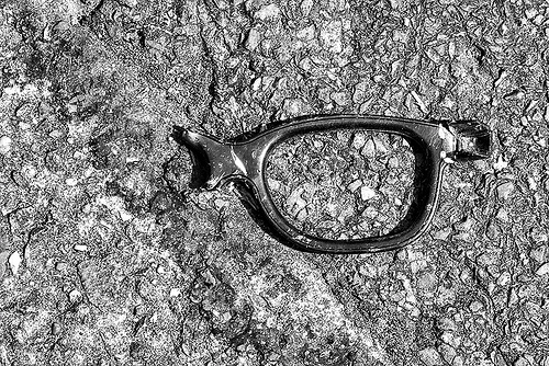 A broken pair of glasses on a patch of rough pavement.
