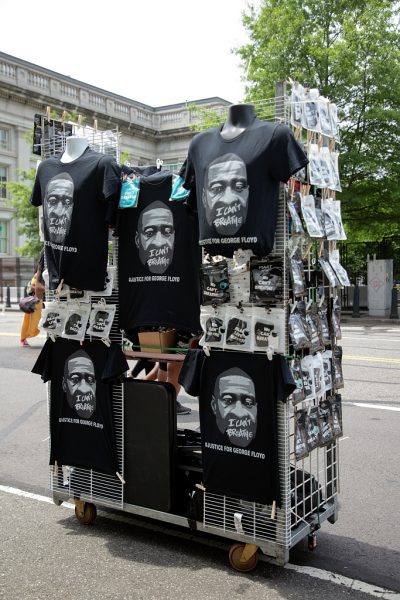 A photograph of a rack of black t-shirts printed with George Floyd’s face, “I CAN’T BREATHE,” and “#JUSTICE FOR GEORGE FLOYD” on the sidewalk at a Washington, D.C. protest.
